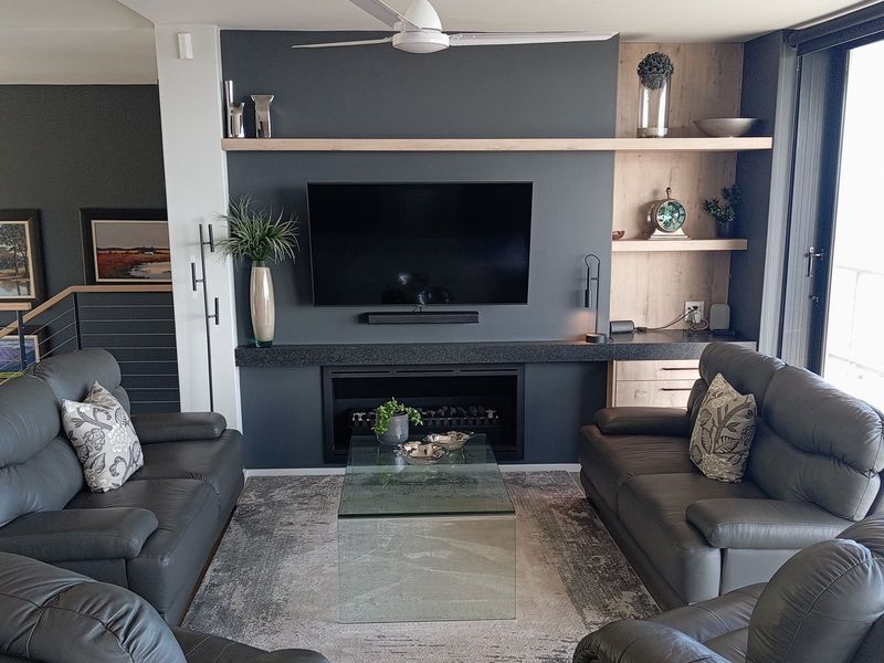Modern living room featuring a dark feature wall with a built-in fireplace, floating timber shelving, and direct access to an outdoor area.