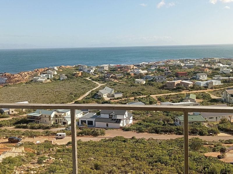 Elevated coastal view overlooking a residential neighborhood and the ocean, framed by a modern stainless steel cable railing.