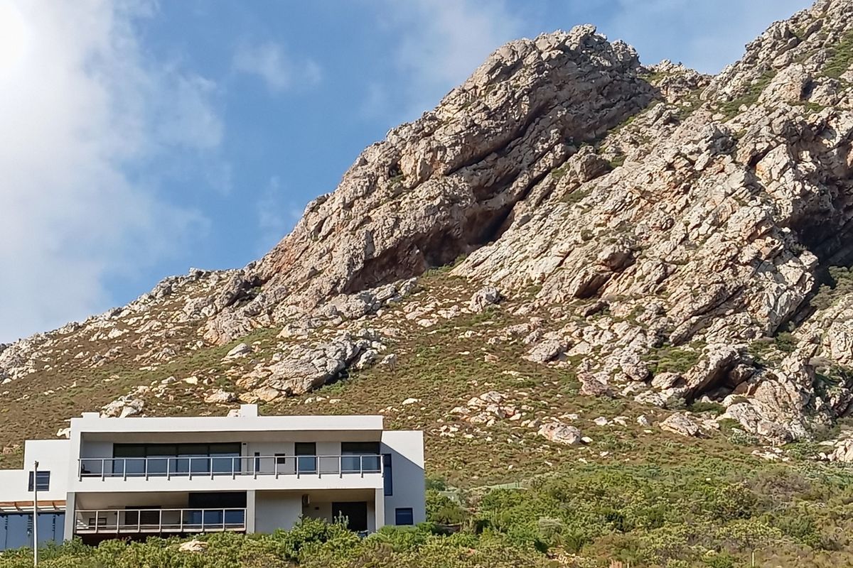 Modern multi-level residence featuring expansive balconies and glass balustrades, set against a dramatic mountain backdrop.