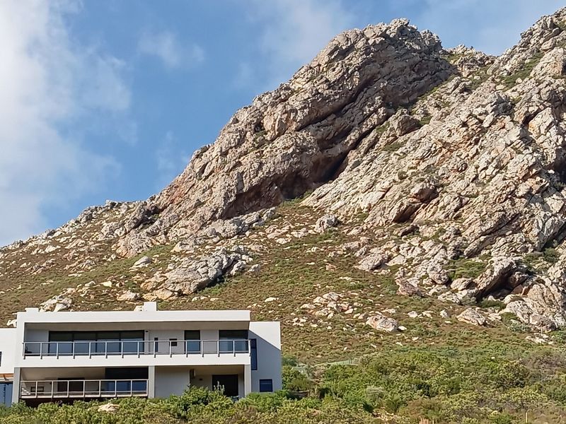 Modern multi-level residence featuring expansive balconies and glass balustrades, set against a dramatic mountain backdrop.