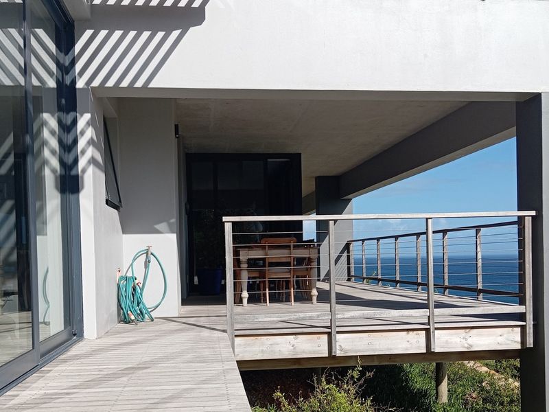 A spacious covered timber deck featuring stainless steel cable railings and direct access to the interior through large sliding glass doors with ocean views.