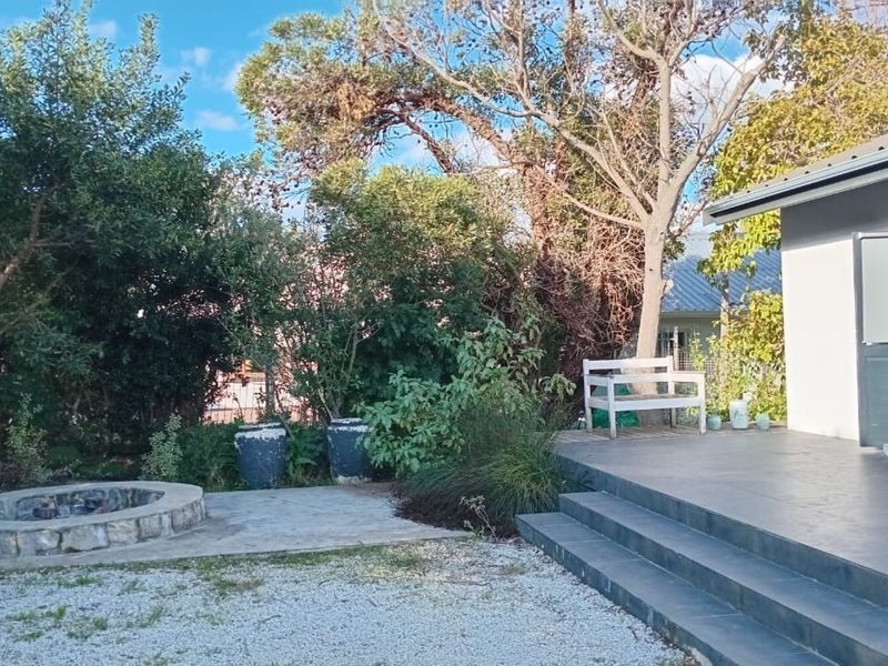 A rear garden area featuring a stone fire pit, gravel landscaping, and a tiled patio with steps leading to the main dwelling.