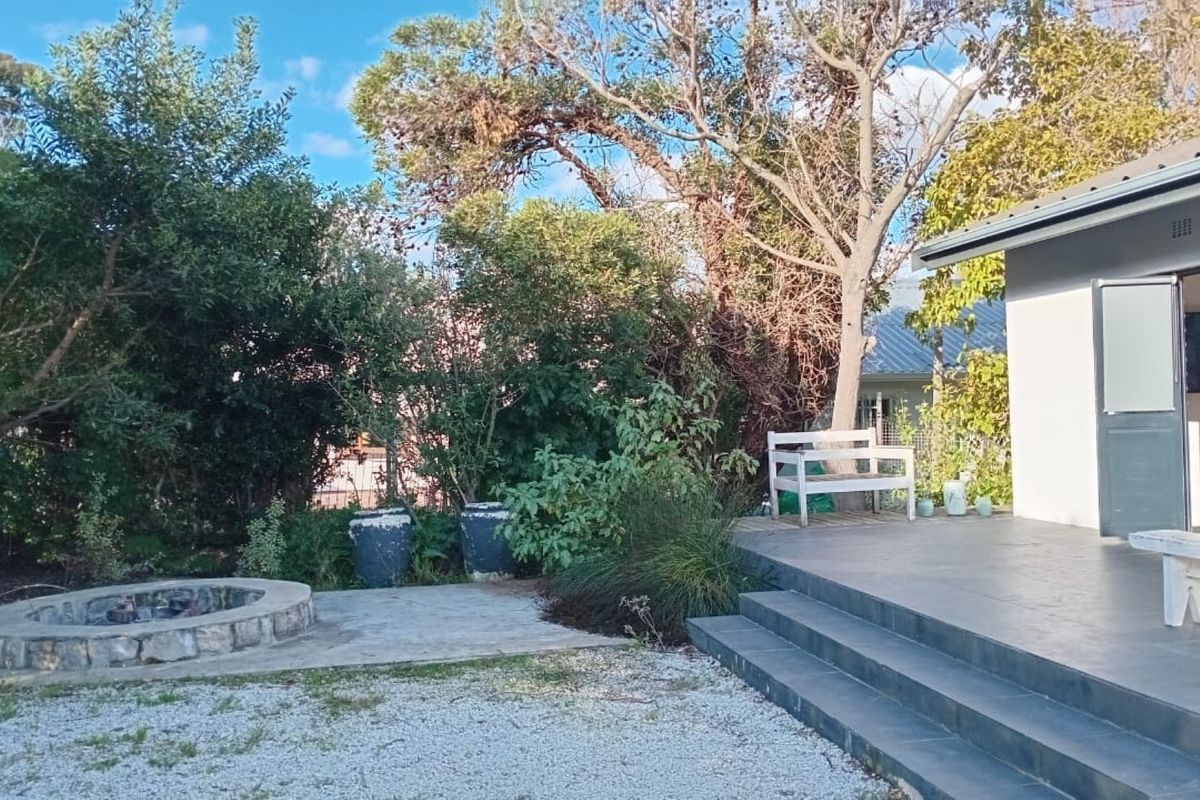 A rear garden area featuring a stone fire pit, gravel landscaping, and a tiled patio with steps leading to the main dwelling.