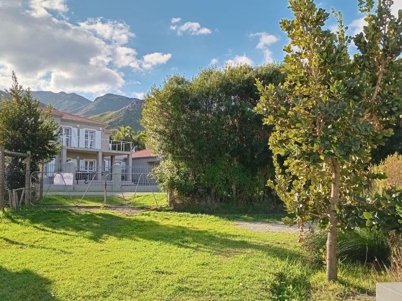 A spacious garden area featuring established trees, lawn, and perimeter fencing with a metal gate, offering views of the surrounding mountain landscape.