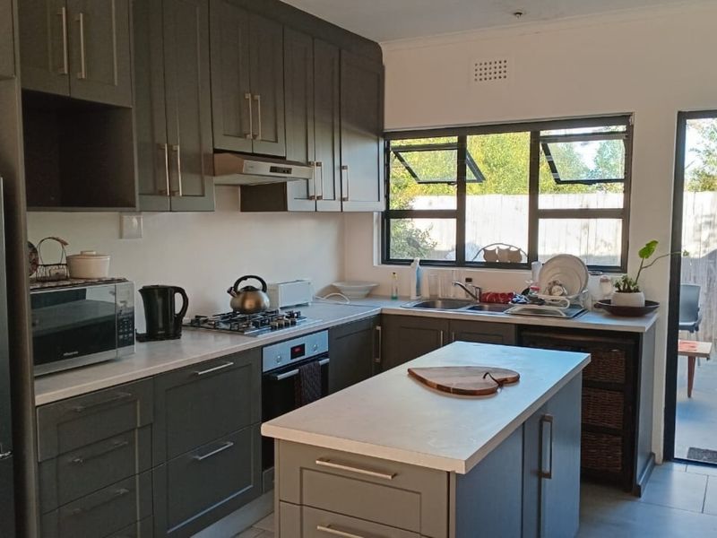 Modern kitchen featuring dark grey cabinetry, a central island, gas hob, built-in oven, and direct access to an outdoor patio area.