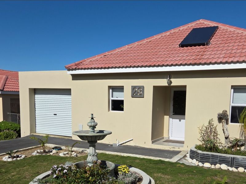Front elevation of a single-story house featuring a tiled roof with solar water heating, a garage, and a landscaped front garden.