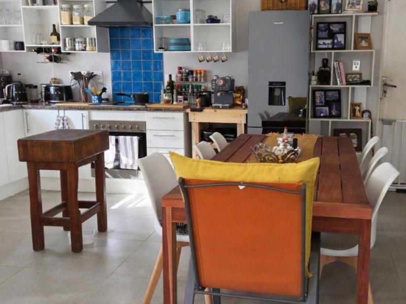 Open-plan kitchen and dining area featuring white cabinetry, blue tiled splashback, integrated oven, and tiled flooring.