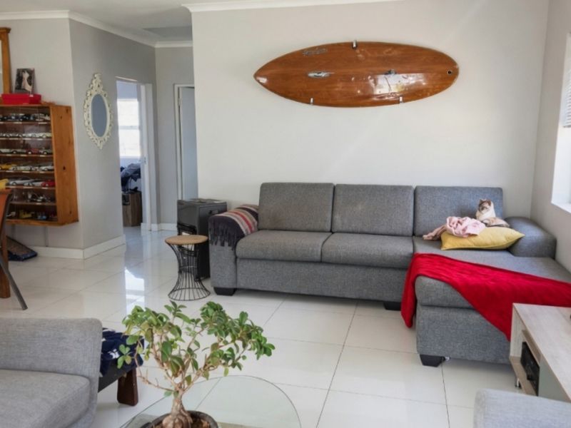 A bright living room featuring neutral tiled flooring, clean wall finishes, and natural light through a side window.