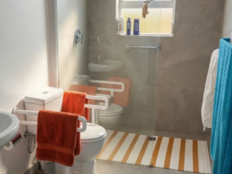 A functional bathroom featuring a pedestal sink, toilet, and a walk-in shower area with glass screen and safety grab rails.