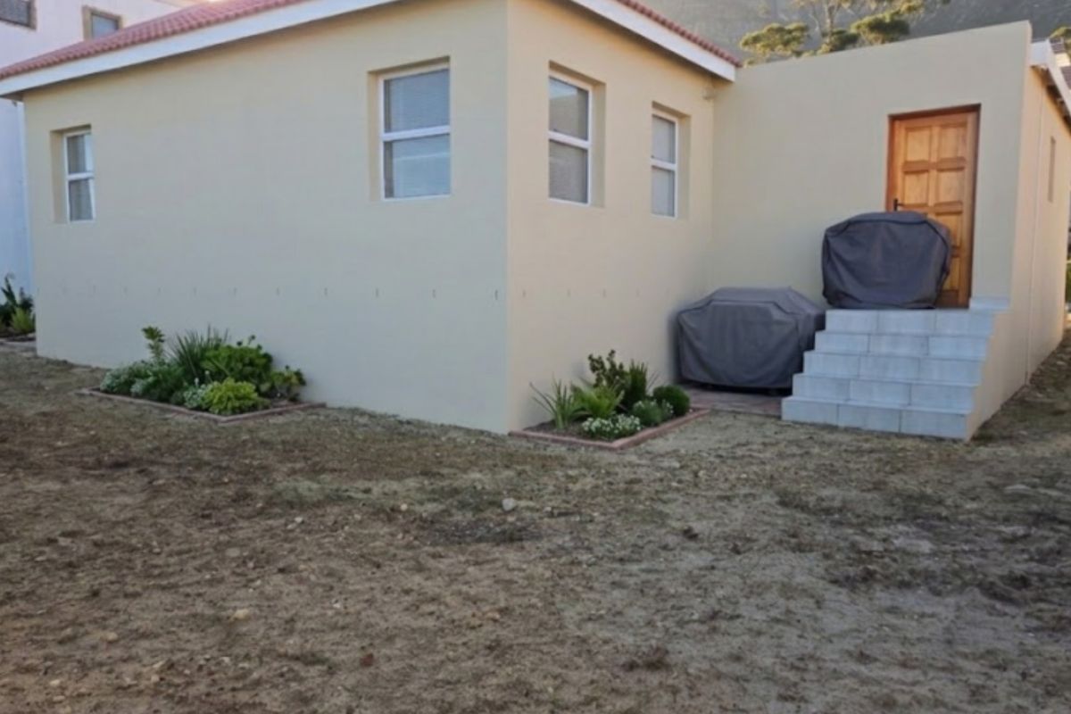 Rear exterior view of the property featuring a tiled entrance staircase, timber door, and established garden beds set against a neutral rendered facade.