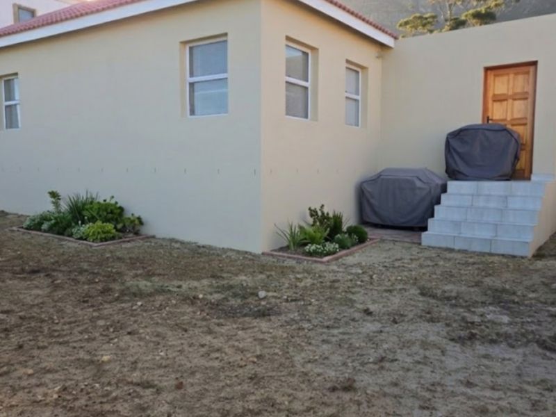 Rear exterior view of the property featuring a tiled entrance staircase, timber door, and established garden beds set against a neutral rendered facade.