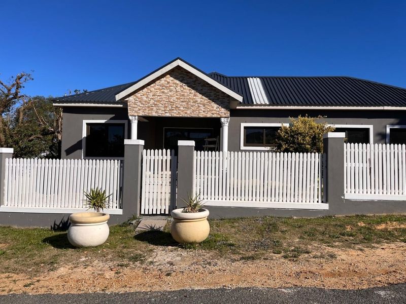 Front elevation of a modern house featuring a gabled entrance with stone cladding, metal roofing, and a white picket fence.