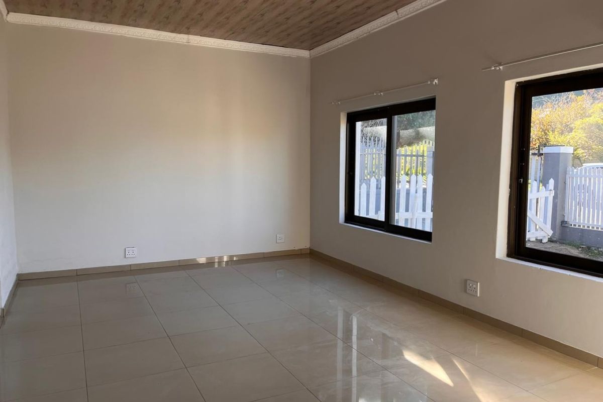 A bright, empty living room featuring neutral tiled flooring, coved ceilings, and large aluminium-framed windows allowing for ample natural light.