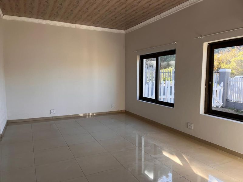 A bright, empty living room featuring neutral tiled flooring, coved ceilings, and large aluminium-framed windows allowing for ample natural light.