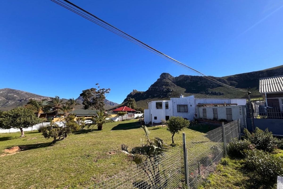 A spacious rear garden area featuring a wire mesh fence, established trees, and scenic mountain views in a quiet residential setting.
