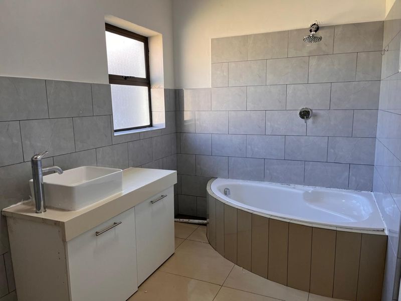 A functional bathroom featuring a vessel sink vanity, built-in bathtub with shower head, and grey wall tiling. Requires minor finishing touches to complete the installation.