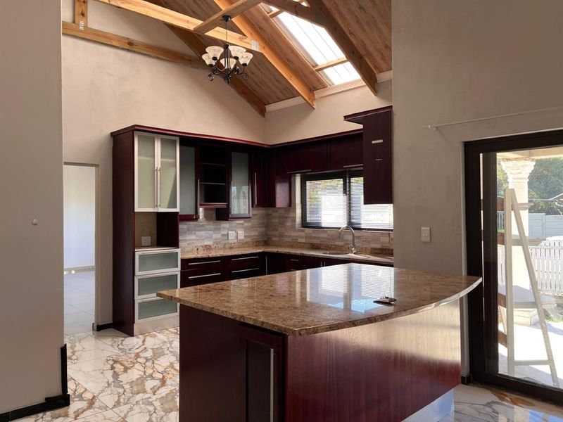 Spacious kitchen featuring a large granite island, timber vaulted ceilings with a skylight, and dark wood cabinetry, offering a bright and open layout.