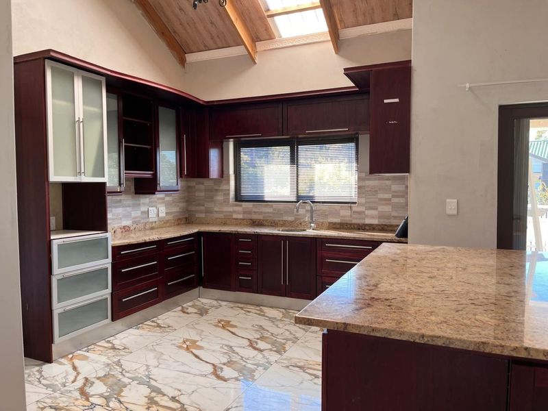 Spacious kitchen featuring dark wood cabinetry, granite countertops, marble-look flooring, and a vaulted ceiling with a skylight, offering a bright and open layout.