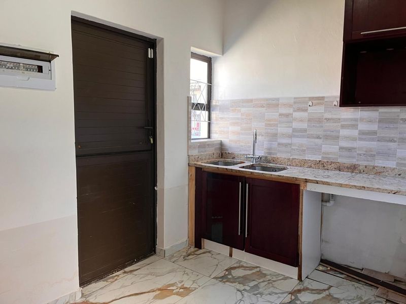 A functional kitchen area featuring a double sink, granite countertops, tiled backsplash, and built-in cabinetry, with some minor finishing work required.