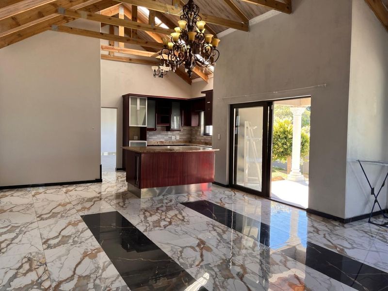 Spacious open-plan living and kitchen area featuring high vaulted timber ceilings, striking marble-effect flooring, and direct access to an outdoor patio.