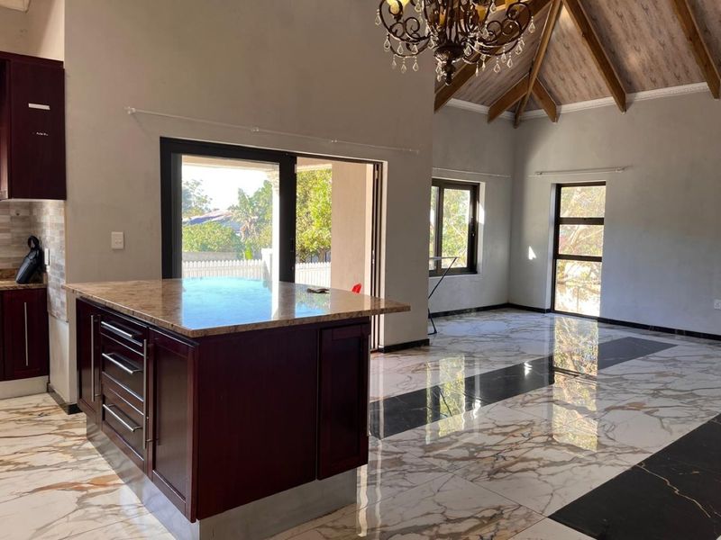 Spacious open-plan living and kitchen area featuring high vaulted ceilings with exposed beams, polished marble-look flooring, and a central kitchen island.