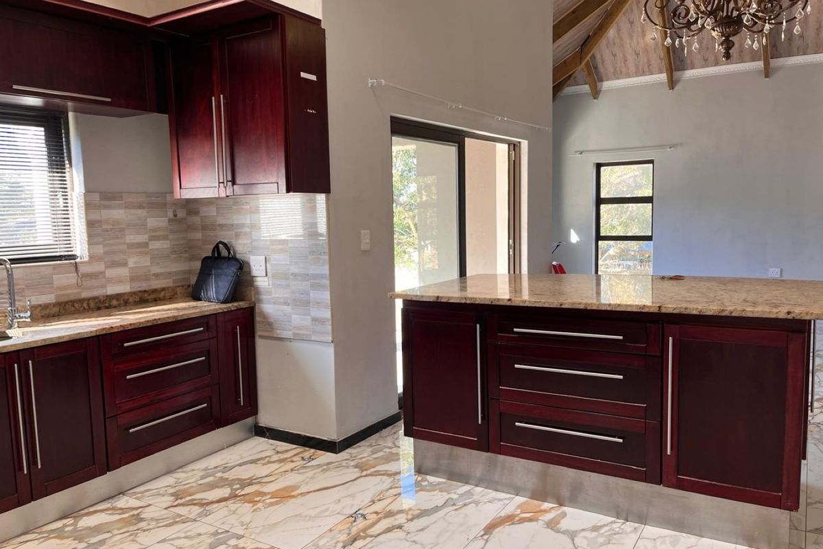 Modern kitchen featuring dark wood cabinetry, granite countertops, a central island, and elegant marble-look tiled flooring under a high vaulted ceiling.