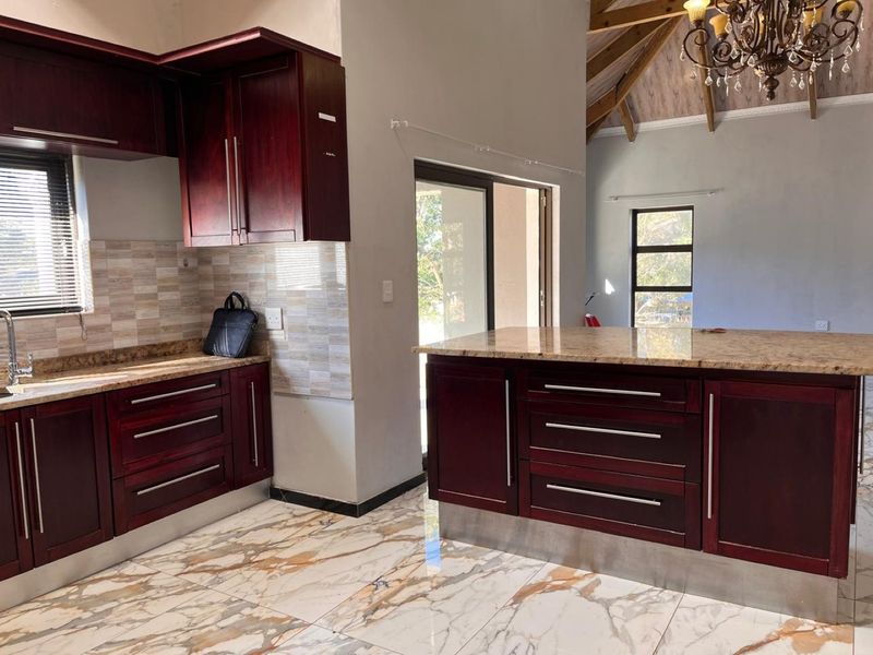 Modern kitchen featuring dark wood cabinetry, granite countertops, a central island, and elegant marble-look tiled flooring under a high vaulted ceiling.