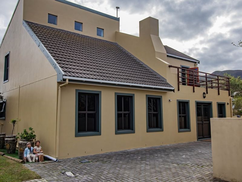 A well-maintained two-story house exterior featuring a tiled roof, chimney, paved driveway, and an upper-level balcony with wooden railings.