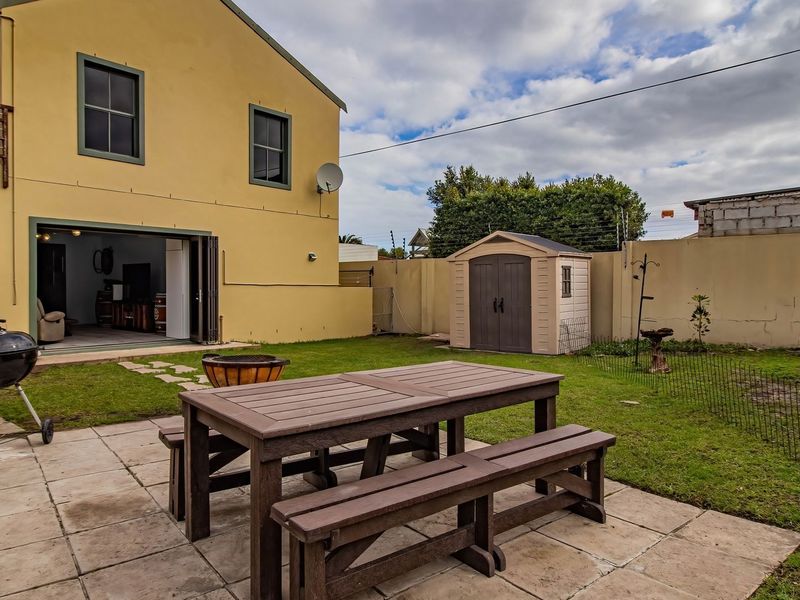 Rear exterior view featuring a paved patio area, lawn, boundary wall with electric fencing, and a storage shed.