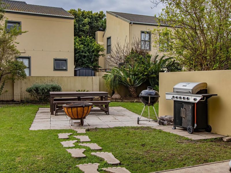 A private rear garden featuring a paved patio area, lawn, and boundary wall, providing a functional outdoor space for relaxation and entertainment.