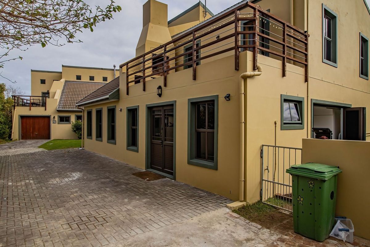 Rear view of the property featuring a paved driveway, a balcony with timber railings, and a chimney, showcasing the exterior building structure.