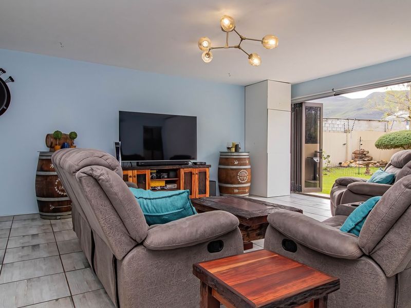 A comfortable living room featuring tiled flooring, a modern chandelier, and large bi-fold doors that open to the rear garden.