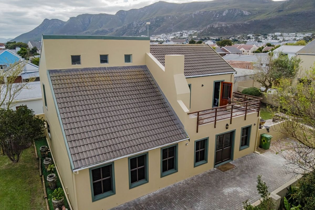 Aerial view of a two-story residential property featuring a tiled roof, upper-level balcony, and paved driveway set against a mountain backdrop.