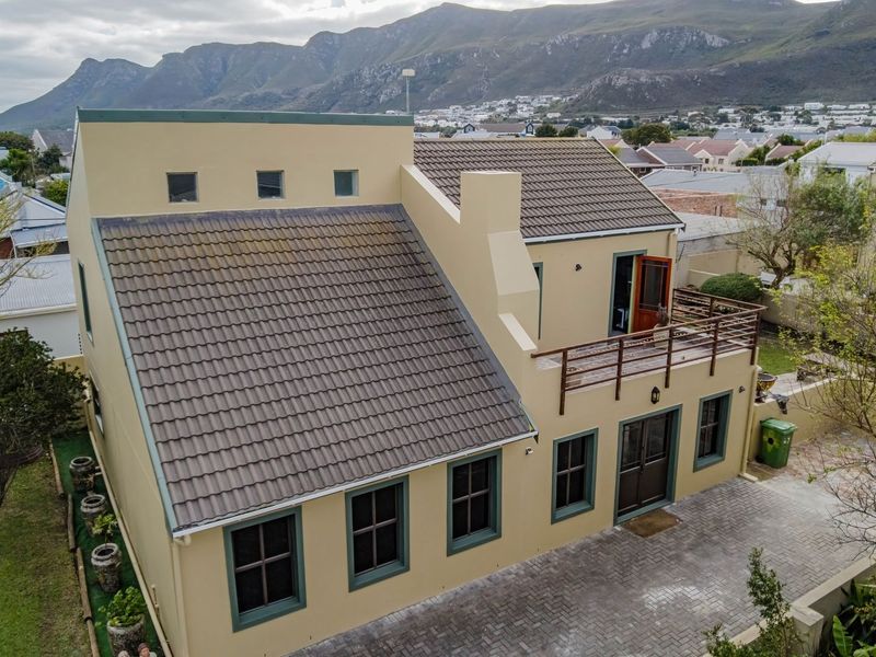Aerial view of a two-story residential property featuring a tiled roof, upper-level balcony, and paved driveway set against a mountain backdrop.