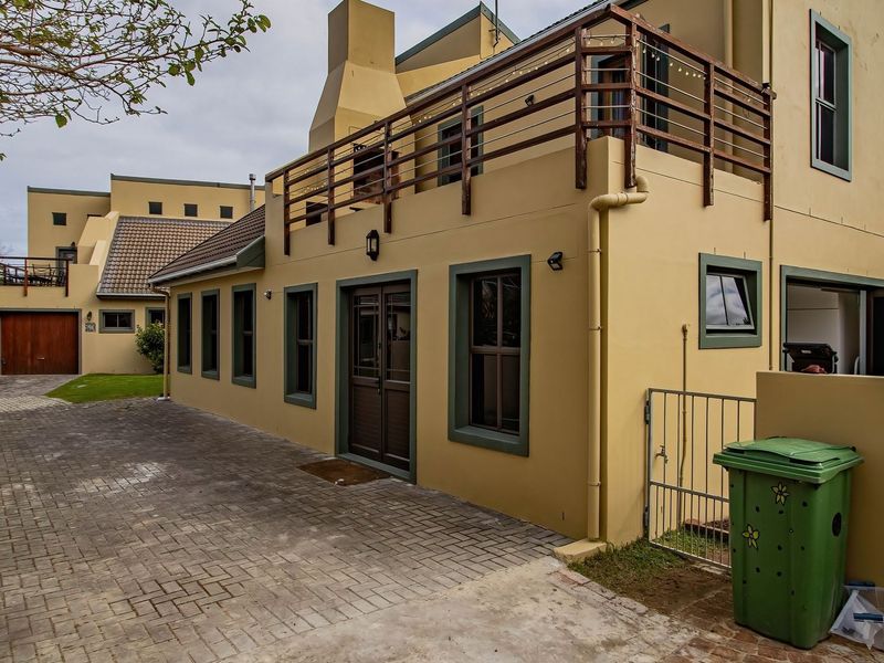Rear view of the property featuring a paved driveway, a balcony with timber railings, and a chimney, showcasing the exterior building structure.
