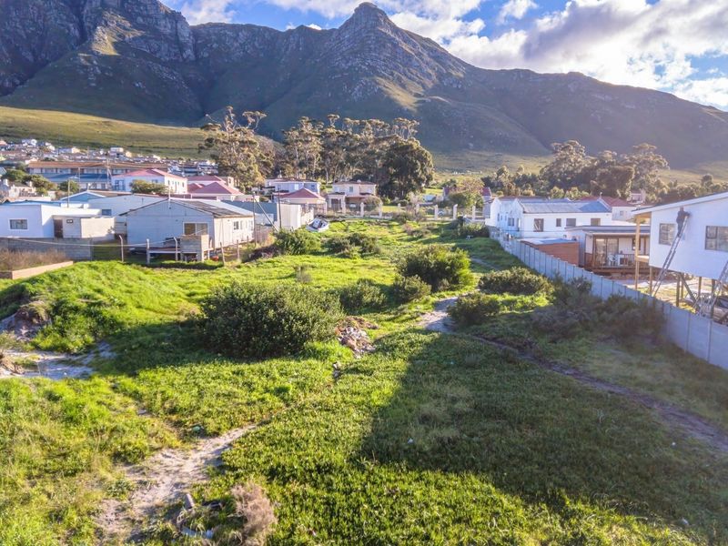 An aerial view of a vacant residential plot situated in a developed neighborhood with mountain views in the background.