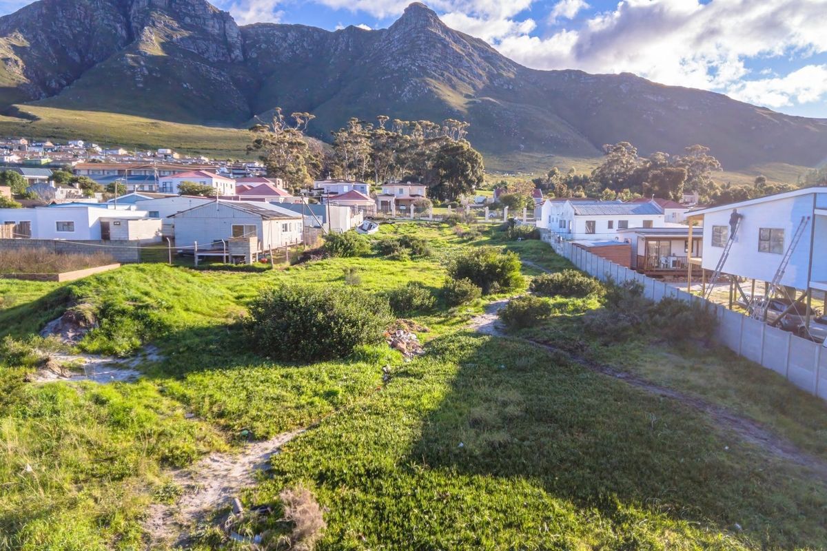 An aerial view of a vacant residential plot situated in a developed neighborhood with mountain views in the background.