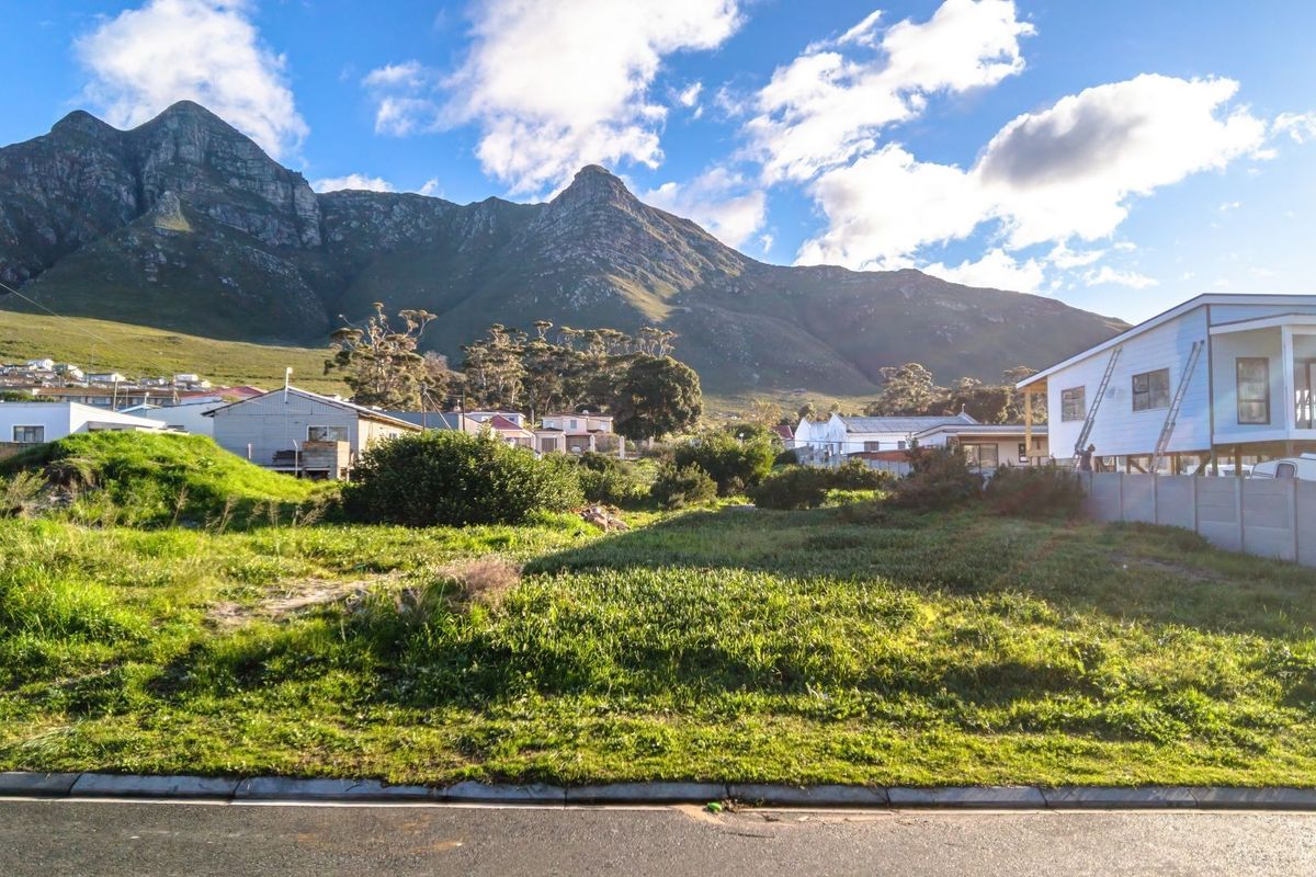 A vacant residential plot of land featuring natural grass cover, situated in a scenic area with mountain views and surrounding residential properties.