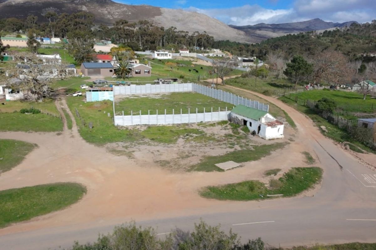 Aerial view of a vacant residential plot featuring a precast concrete boundary wall and a small, dilapidated outbuilding structure.