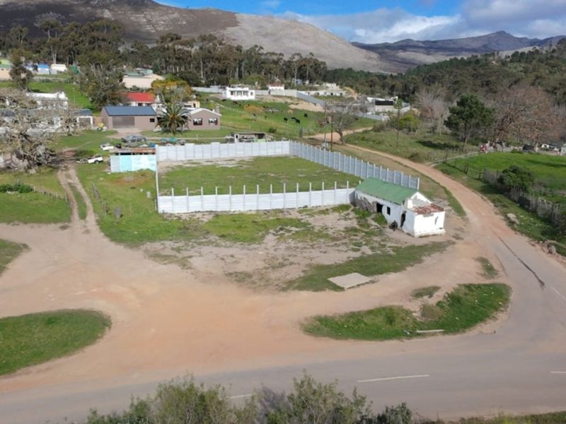 Aerial view of a vacant residential plot featuring a precast concrete boundary wall and a small, dilapidated outbuilding structure.