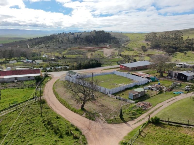 Aerial view of a vacant residential plot enclosed by a perimeter wall, situated in a rural landscape with surrounding infrastructure.