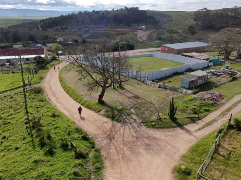 Aerial view of a vacant residential plot featuring perimeter precast concrete walling and access via a dirt road in a rural setting.