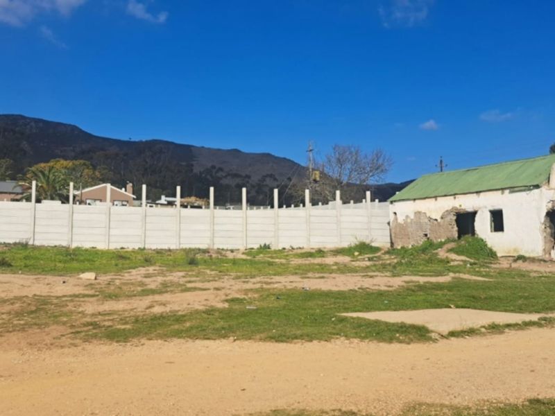 Vacant residential land featuring a dilapidated masonry structure and a precast concrete boundary wall with mountain views in the background.