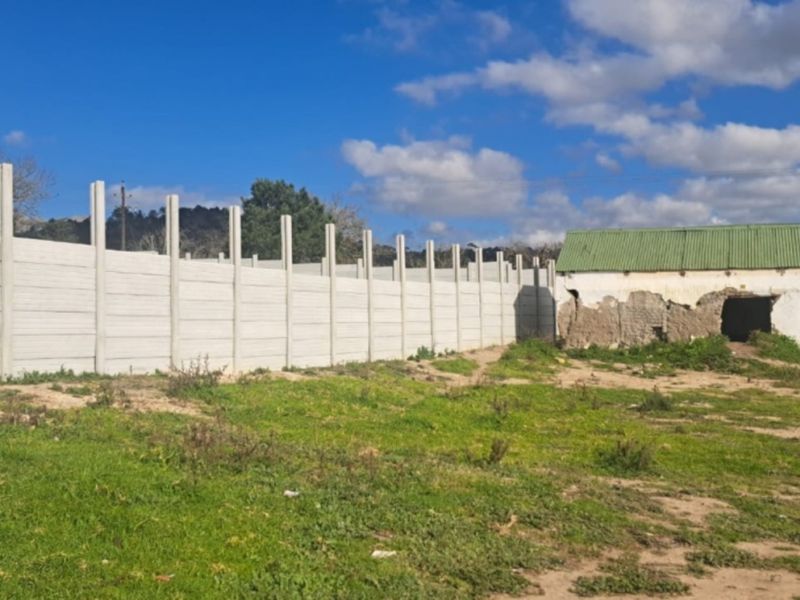 Vacant residential land featuring a long precast concrete boundary wall and a dilapidated masonry structure with a corrugated metal roof.