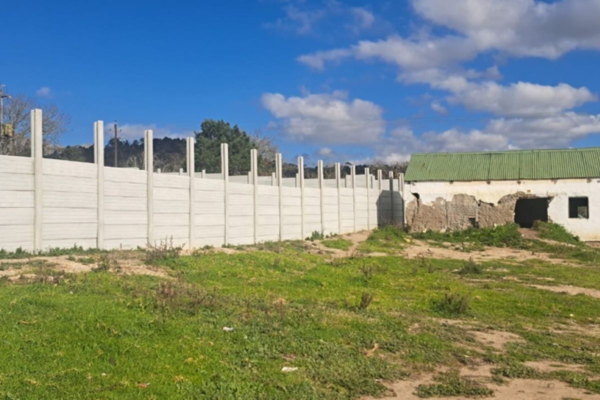 Vacant residential land featuring a long precast concrete boundary wall and a dilapidated masonry structure with a corrugated metal roof.