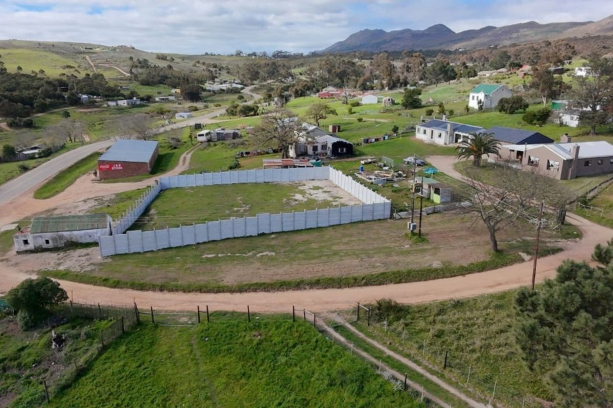 Aerial view of a vacant residential plot enclosed by precast concrete walling, situated in a rural landscape with surrounding properties and mountain views.