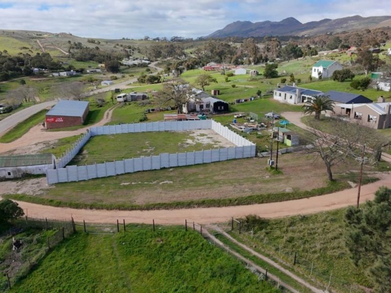Aerial view of a vacant residential plot enclosed by precast concrete walling, situated in a rural landscape with surrounding properties and mountain views.