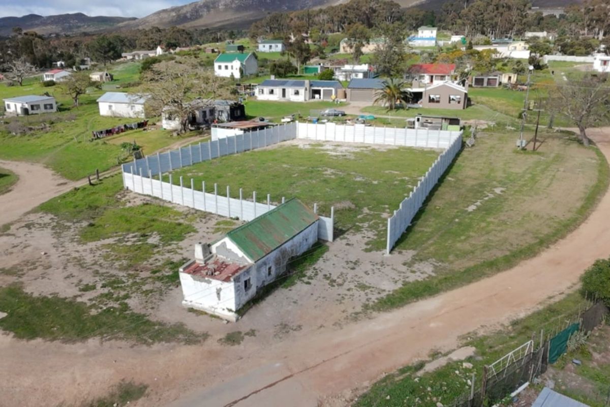 Aerial view of a vacant residential plot featuring a precast concrete boundary wall and a small, dilapidated existing structure on the property.