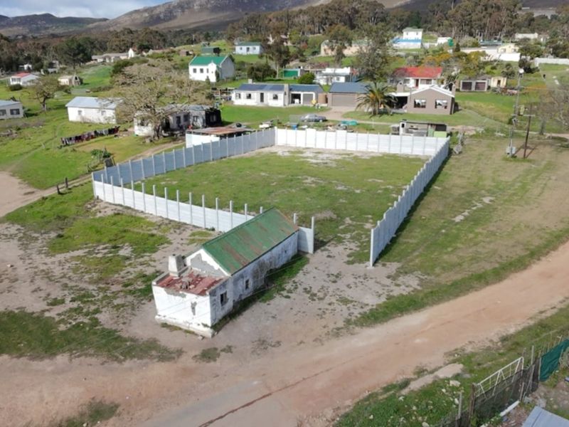 Aerial view of a vacant residential plot featuring a precast concrete boundary wall and a small, dilapidated existing structure on the property.