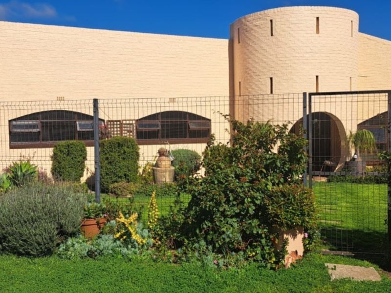 Front view of a unique house featuring a distinctive turret design, brick exterior, and a well-maintained garden enclosed by security fencing.